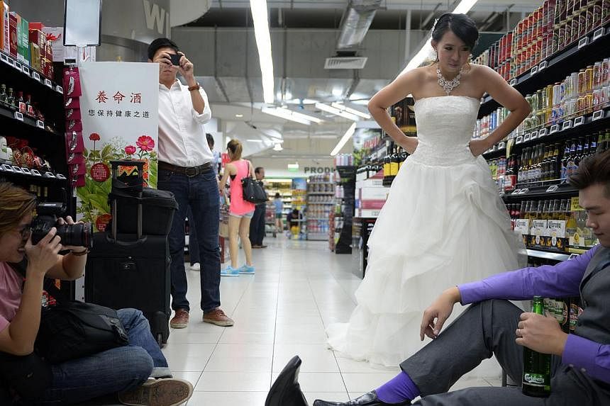 Mr Smith Leong, 30, and his fiancee Chris Goh, 29, pictured during their wedding shoot with photographer Ma Xianrong (left), 30, at the FairPrice outlet in City Square Mall yesterday. -- ST PHOTO: MARK CHEONG