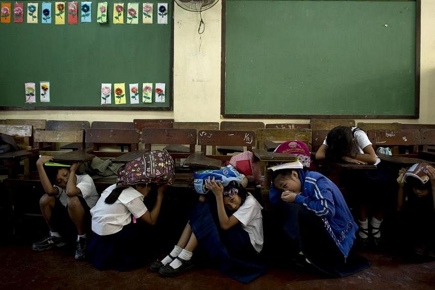 Students of Bagong Silangan Elementary school cover their head during an earthquake drill in Manila on March 19, 2014. A series of moderate earthquakes and aftershocks hit the Philippines early Sunday, with US geologists estimating the shallowest –