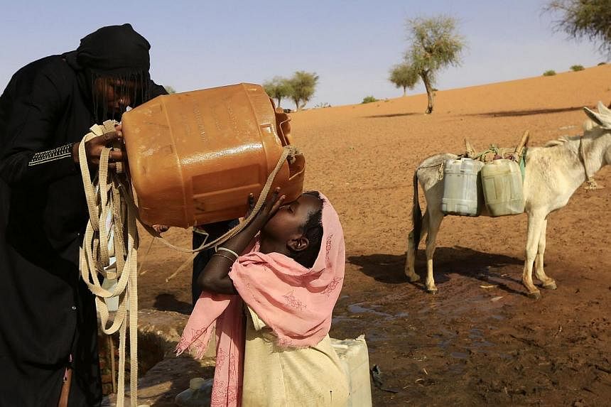 A girl is helped by her sister as she drinks water in Mellit town in North Darfur on March 24, 2014.&nbsp;Singaporeans can now help people in regions such as Africa, South Asia and Central America get clean water and sanitation, just by making an onl