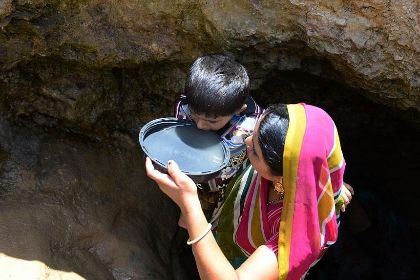 An Indian villager offers drinking water collected from a man-made well to her son in the Sujangadh village of Surendranagar district, some 160 kms from Ahmedabad on June 1, 2014.&nbsp;Two important water events are taking place in Singapore over the