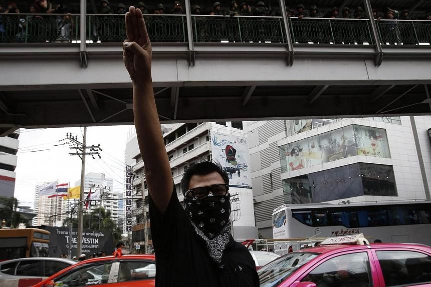 A protester against military rule gestures by holding up his three middle fingers in the air, as soldiers look on from an elevated walkway, during a brief demonstration outside a shopping mall in Bangkok on June 1, 2014. -- PHOTO: REUTERS