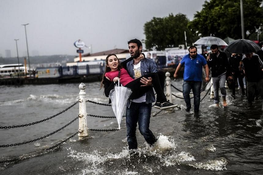 A Turkish man carries a woman through a flooded quay on June 2, 2014, at Uskudar district of Istanbul during a rainy day. -- PHOTO: AFP