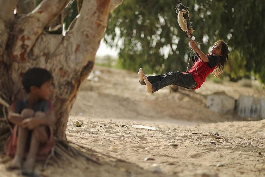 A Palestinian girl swings on a rope tied on a tree at a former Jewish settlement in Khan Younis in the southern Gaza Strip June 3, 2014. -- PHOTO: REUTERS