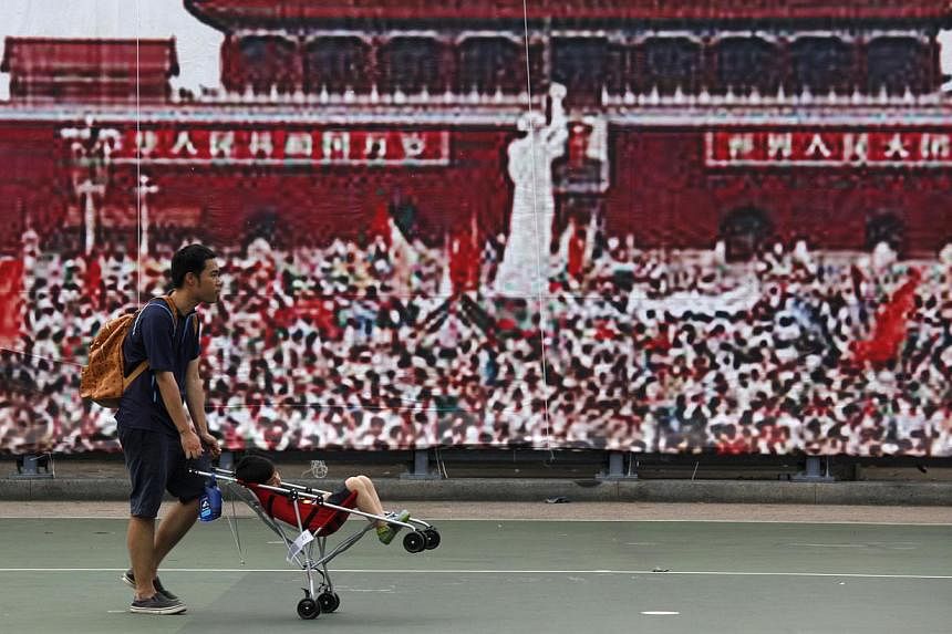 A man and his child pass by a backdrop showing a pro-democracy movement at Beijing's Tiananmen Square in 1989, at Hong Kong's Victoria Park on June 3, 2014. -- PHOTO: REUTERS