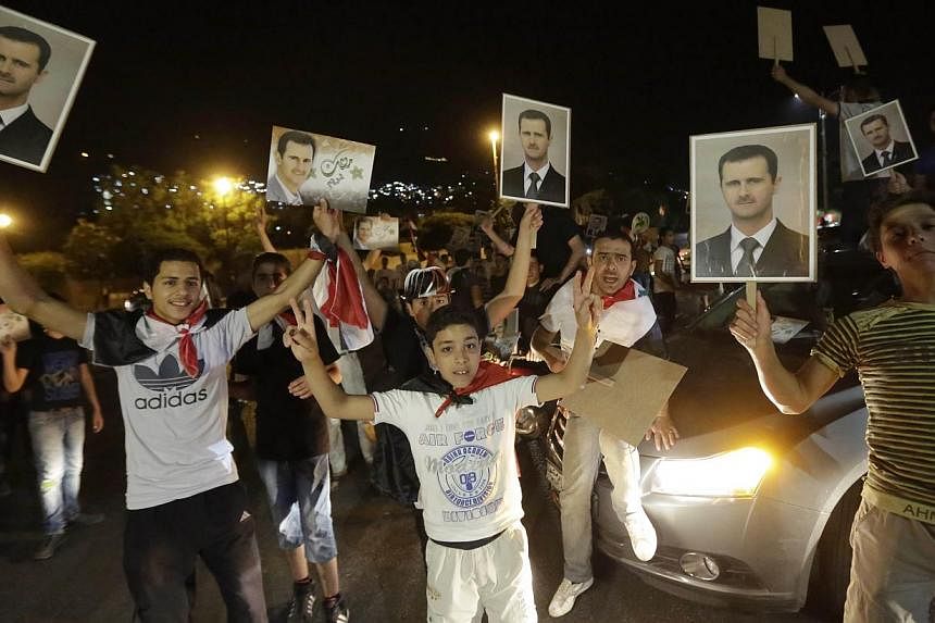 Syrians hold pictures of re-elected Syrian President Bashar al-Assad as they celebrate in Damascus after Mr Assad was announced as the winner of the country's presidential elections on June 4, 2014. -- PHOTO: AFP