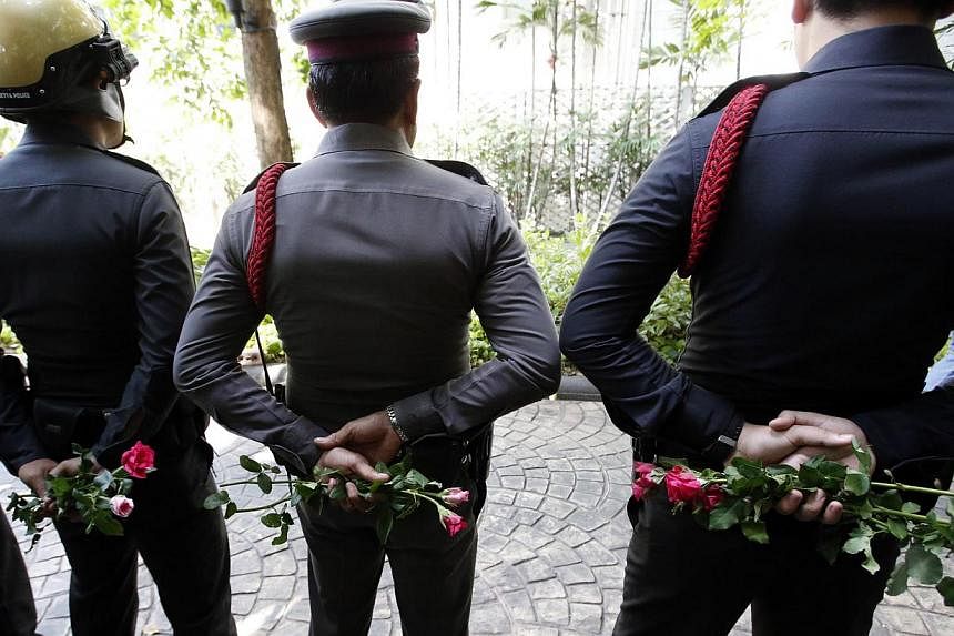 Thai policemen hold roses given by pro-army supporters behind their back as they stand guard outside the Australian embassy in Bangkok on June 4, 2014. -- PHOTO: REUTERS