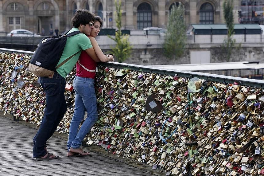A couple stands on the Pont des Arts in front of padlocks hitched by lovers&nbsp;in Paris&nbsp;on Aug 30, 2013. -- PHOTO: AFP