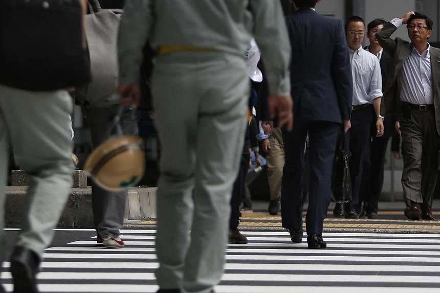 A man scratching his head crosses a street at a business district in Tokyo May 20, 2014. Japan's economy saw its strongest expansion in more than two years during the first quarter of 2013, revised data showed Monday, but a sales tax rise has weighed