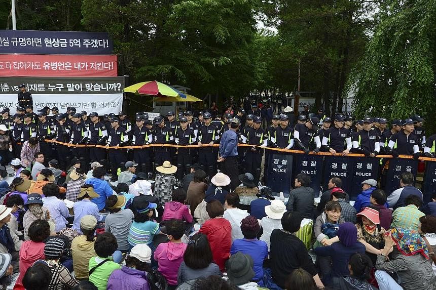 South Korean policemen stand guard in front of the main gate of the Evangelical Baptist Church premises, as church believers sit in front of the police barricade, in Anseong on June 11, 2014. South Korean police raided the religious commune seeking t