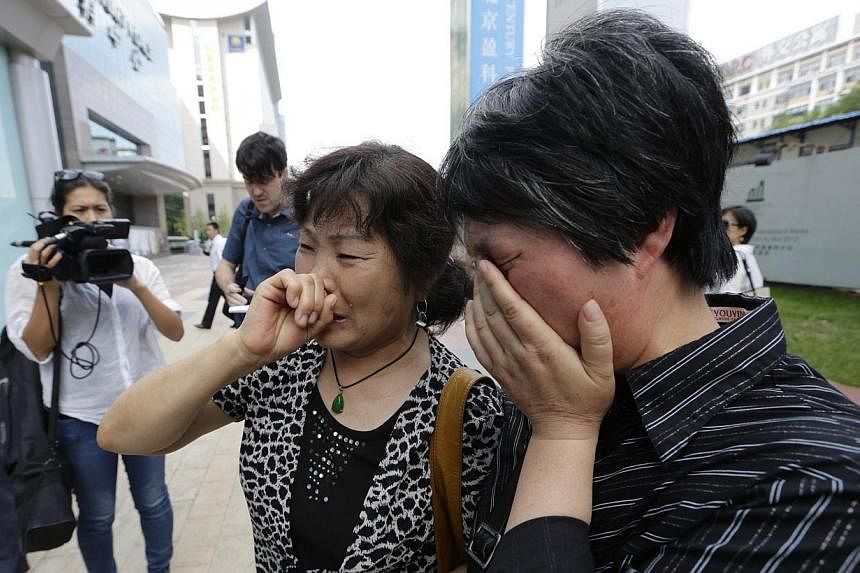 A woman (left), whose son, daughter-in-law and grandson were aboard the missing Malaysia Airlines flight MH370, cries after she and other family members failed to express their appeals to the airline outside its office in Beijing on June 11, 2014.&nb