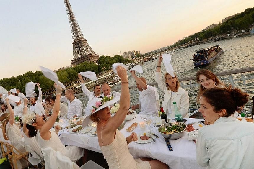 Participants enjoy their meal during a "Diner en Blanc" ('Dinner in White'), the world’s only viral culinary event, a chic secret pop-up style picnic phenomenon originally started in France, on a bridge over the Seine river in Paris on June 12, 201