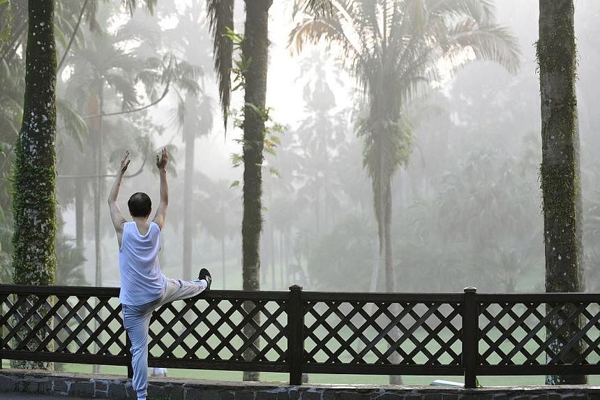 A man performing a series of stretching exercises while beyond him, morning mist shrouds an area of the Singapore Botanic Gardens on 2 June 2011. -- PHOTO: ST FILE