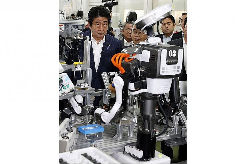 Japanese Prime Minister Shinzo Abe inspects a robot working at an assembly line of cash dispensers at a factory in Kazo, suburban Tokyo on June 19, 2014.&nbsp;Japanese Prime Minister Shinzo Abe wants to stage a "Robot Olympics" in 2020, the same year
