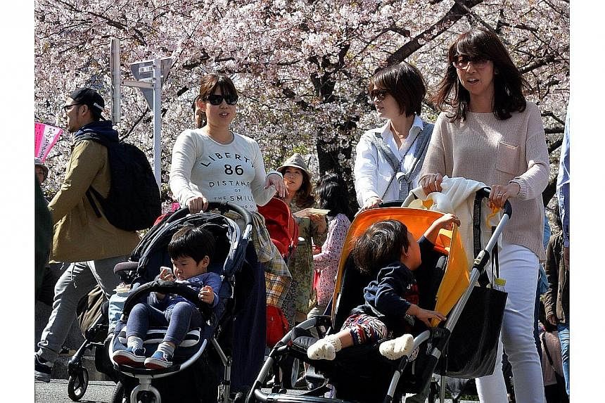Young mothers push their baby strollers under fully bloomed cherry blossom trees along a riverside promenade in Tokyo on April 4, 2014.&nbsp;Sexist jeers from governing party members on Thursday, June 19, 2014, repeatedly interrupted a Tokyo assembly