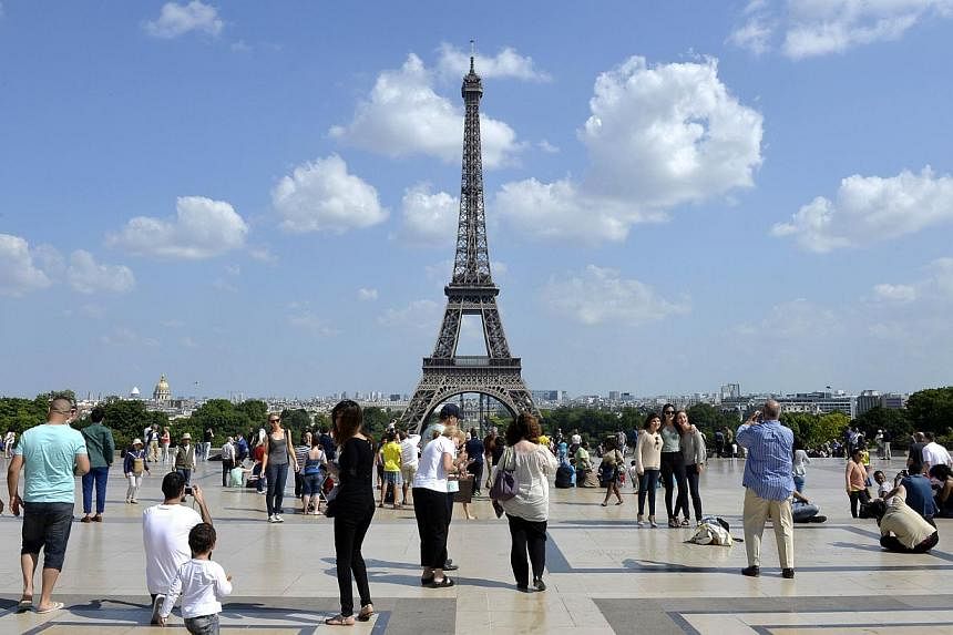 People stand and take photographs at the Human Rights Square in front of the Eiffel tower on a warm and sunny day on June 18, 2014 in Paris. -- PHOTO: AFP