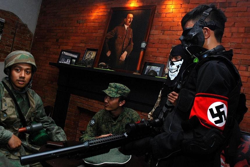 Indonesian customers coming in World War II motif military uniforms, one bearing a Nazi's swastika insignia while a portrait of Adolf Hitler hangs in the background, at the reopened SoldatenKaffee in Bandung city, western Java island on June 21, 2014