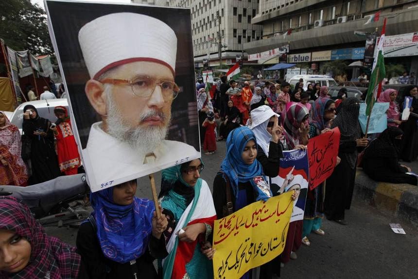 Female supporters of Tahir-ul Qadri carrying his portrait during a protest last week in Karachi. The prominent cleric had been expected to arrive in Islamabad yesterday to lead what he describes as a revolution against Pakistan Prime Minister Nawaz S