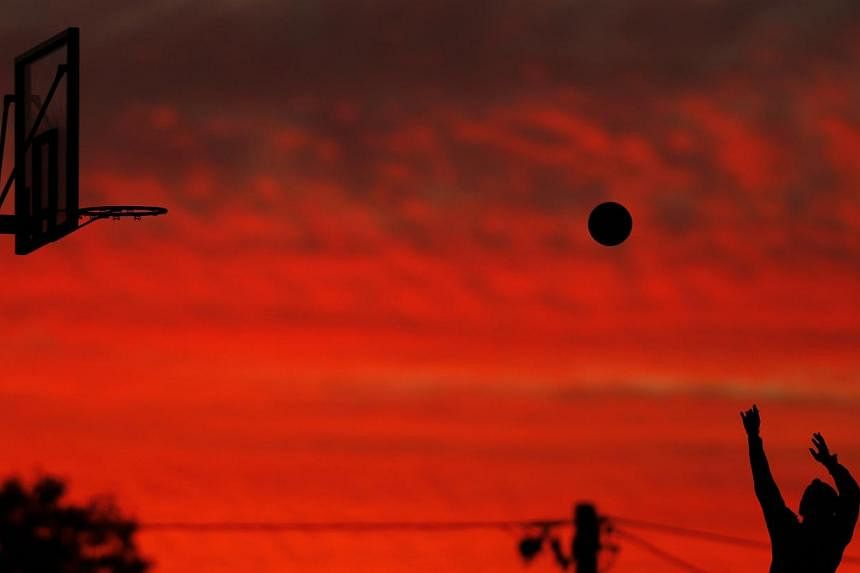A boy throws to the basket as the setting sun illuminates low clouds at an outdoor basketball court in Sydney's beachside suburb of Cronulla, on June 12, 2014.&nbsp;According to Australia's Bureau of Meteorology, Sydney has recorded its warmest May o