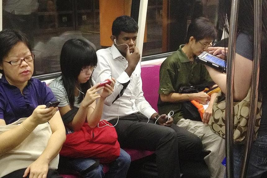 MRT commuters using their mobile devices in a MRT train on Oct 18, 2012. Software piracy is on the wane here partly due to computers falling out of favour with consumers, and the growing popularity of tablets. -- ST PHOTO: FILE