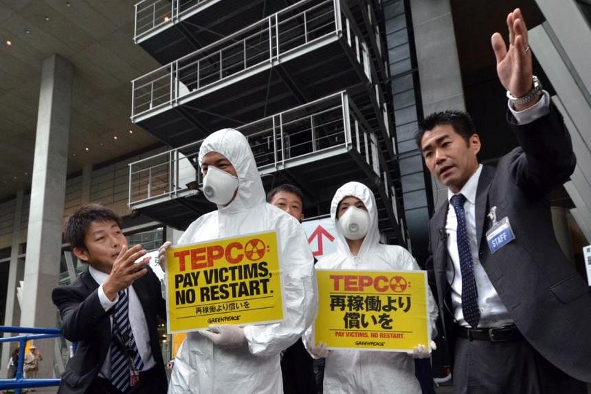Members of environmental group Greenpeace wearing radiation protection suits are asked by Tepco staff to move away from the entrance of a company shareholders' meeting in Tokyo on Thursday. Activists&nbsp;wore full protective suits and industrial fac