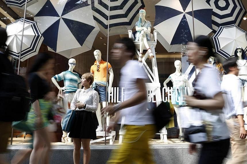 A woman stands in front of a luxury brand store as people walk past at a shopping district in Tokyo on June 26, 2014. -- PHOTO: REUTERS