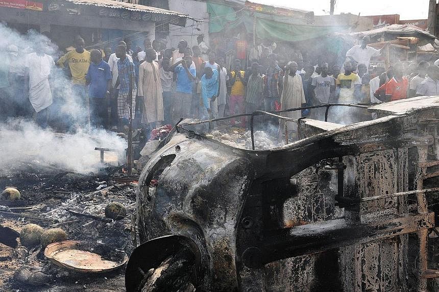 People gather to look at a burnt vehicle following a bomb explosion that rocked the busiest roundabout near the crowded Monday Market in Maiduguri, Borno State, on July 1, 2014.&nbsp;A truck exploded in a huge fireball killing at least 15 people on T