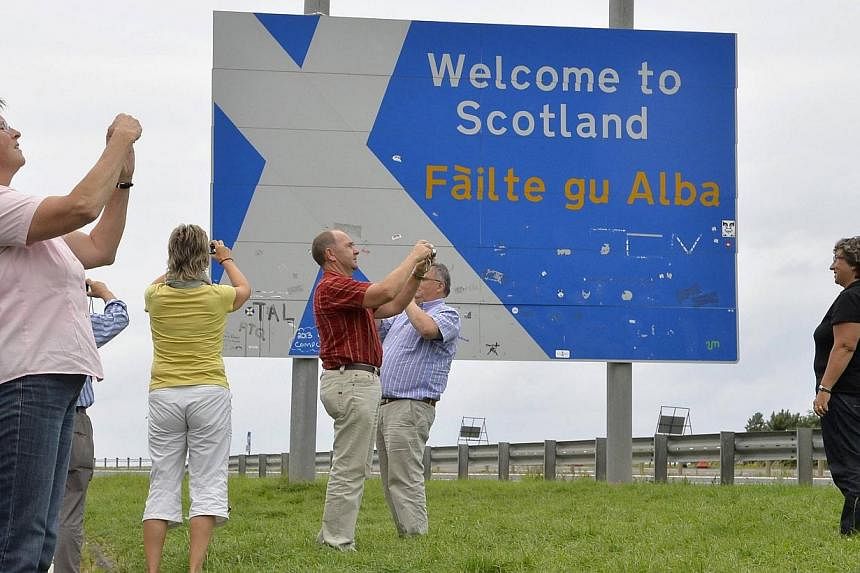 Swiss tourists take photographs next to a road that marks the England - Scotland border, at a lay-by on the A1 road near Berwick in this August 20, 2013 file photo.&nbsp;Support for Scottish independence is falling ahead of a referendum in September,