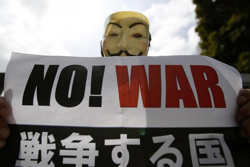 A protester wearing a mask holds a placard at a rally against Japan's Prime Minister Shinzo Abe's push to expand Japan's military role in front of Abe's official residence in Tokyo on July 1, 2014. -- PHOTO: REUTERS&nbsp;