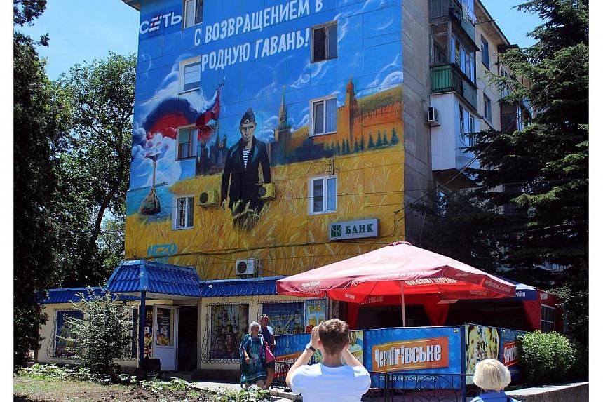 Pedestrians walk by a mural depicting Russian president Vladimir Putin dressed as a Russian Navy seaman, in the Crimean city of Sevastopol, on June 28, 2014.&nbsp;Russia plans to issue a banknote dedicated to Crimea, a senior central bank official sa