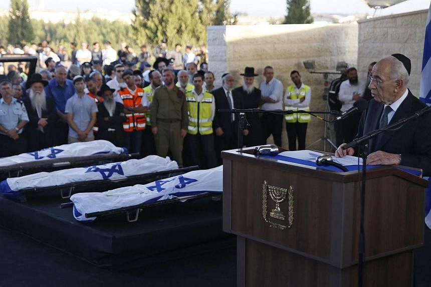 Israeli outgoing President Shimon Peres (right) delivers a speech next to the bodies of Gilad Shaer and Naftali Frenkel, both 16, and 19-year-old Eyal Ifrach, all three wrapped in their national flag, as he attends their funeral on July 1, 2014 in th
