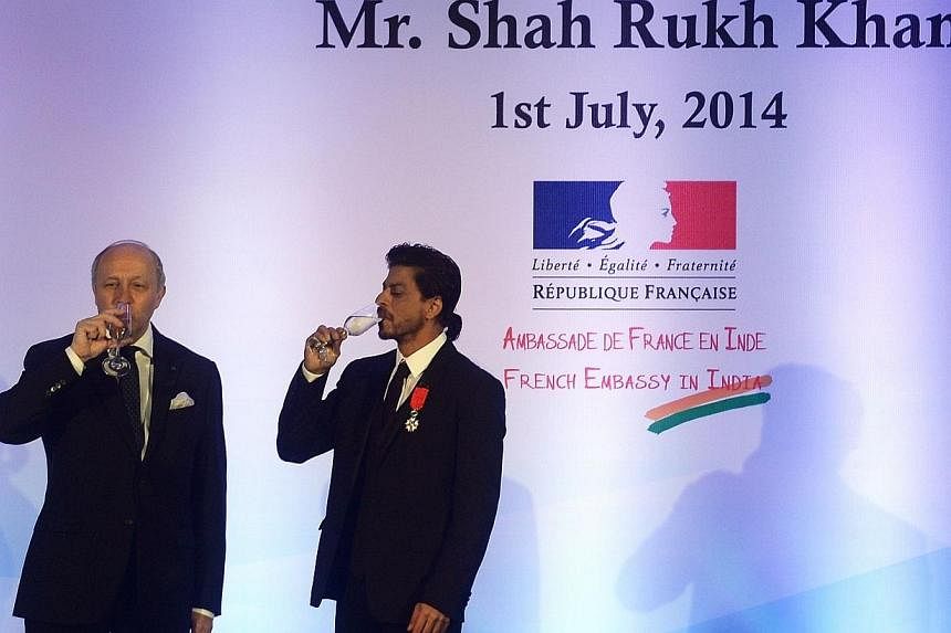French Foreign Minister Laurent Fabius (left) and Bollywood star Shah Rukh Khan sip champagne after Khan was awarded with the Chevalier de la Legion d'Honneur title during a function in Mumbai on July 1, 2014.&nbsp;Bollywood superstar Shah Rukh Khan 
