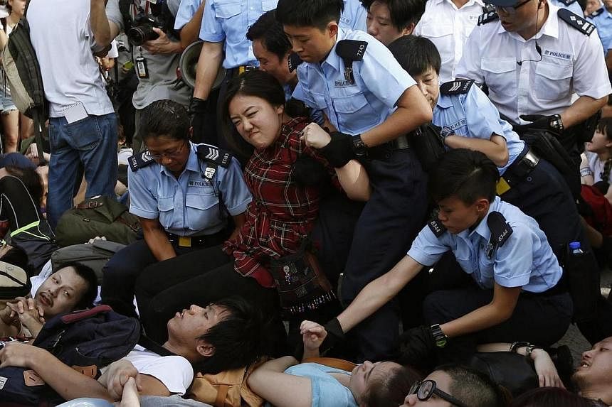 A protester reacts as she is dragged away by police officers on a street outside HSBC headquarters at Hong Kong's financial Central district on Wednesday, July 2, 2014, after an overnight sit-in with fellow demonstrators, at a mass rally demanding gr