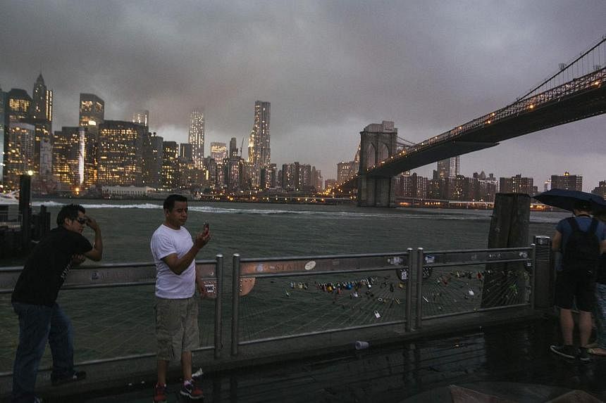 Tourists stand underneath the Brooklyn Bridge to photograph a summer storm bearing down on New York on July 2, 2014. -- PHOTO: REUTERS