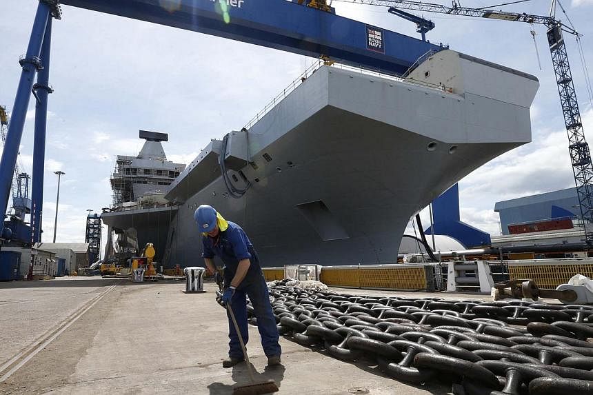 A worker sweeps in front of HMS Queen Elizabeth, the first of two aircraft carriers being built by British defence firm BAE Systems, at the Rosyth Dockyard in Fife, Scotland on June 17, 2014. -- PHOTO: REUTERS
