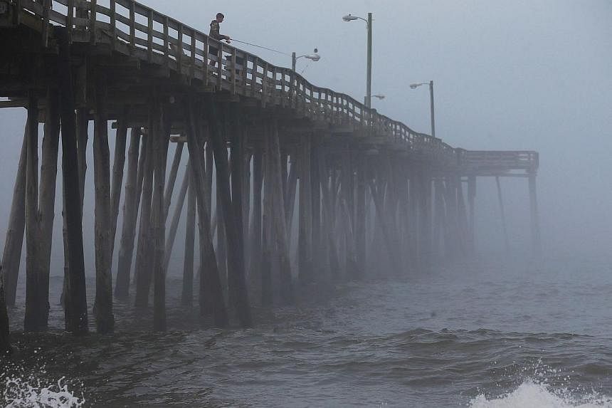 A man fishes from the Nags Head Pier as fog and heavy surf roll in, on July 3, 2014 in Nags Head, North Carolina. Hurricane warning has been issued for North Carolina's Outer Banks due to approaching Hurricane Arthur. -- PHOTO: AFP