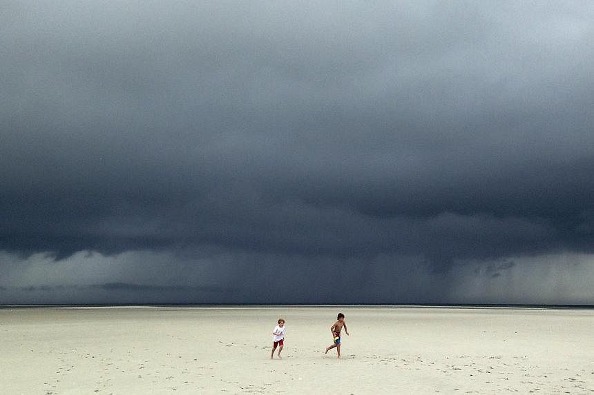 Jack Segar (right) and Finn Harden run across a deserted sandbar beach outside Barnstable Harbor as storm clouds associated with Tropical Storm Arthur pass over Cape Cod Bay behind them in Barnstable, Massachusetts on July 4, 2014. -- PHOTO: REUTERS