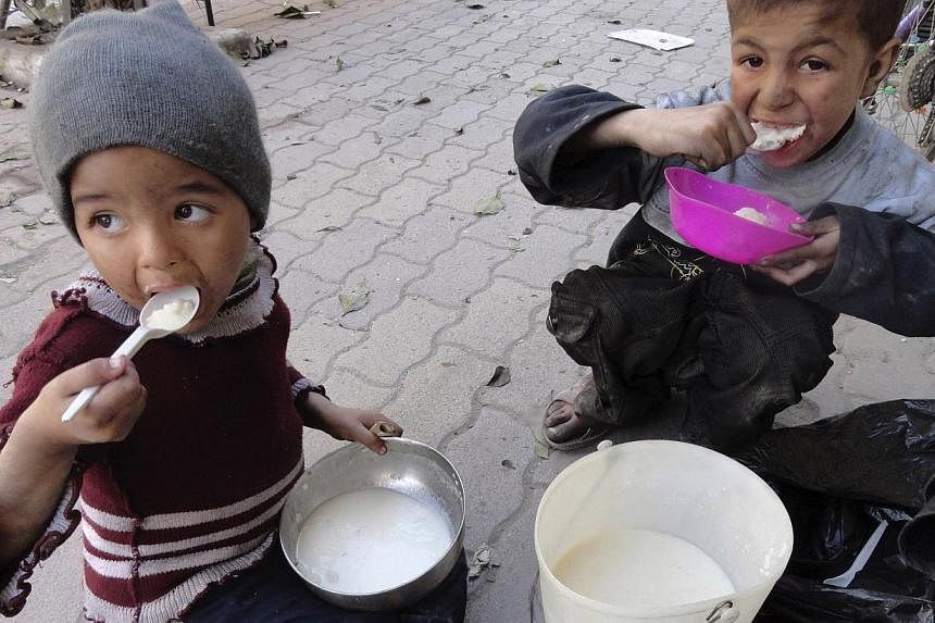 Children eat food distributed to them in the besieged al-Yarmouk camp, south of Damascus, on April 7, 2014. -- PHOTO: REUTERS