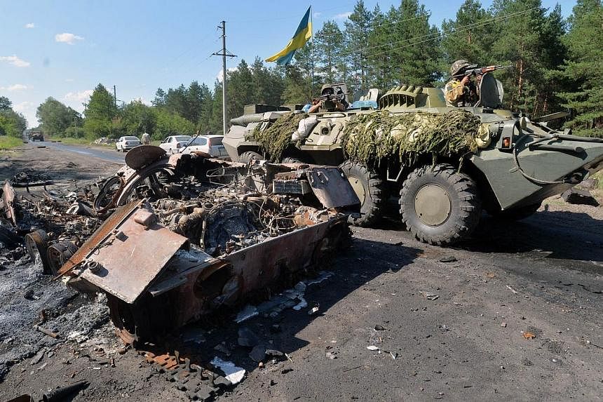 An armoured personnel carrier (APC) bearing the Ukrainian flag drives past a burned APC of pro-Russian militants, outside Nickolayevka, a small eastern Ukrainian city near Slavyansk, on July 5, 2014, two days after the city was taken back by Ukrainia
