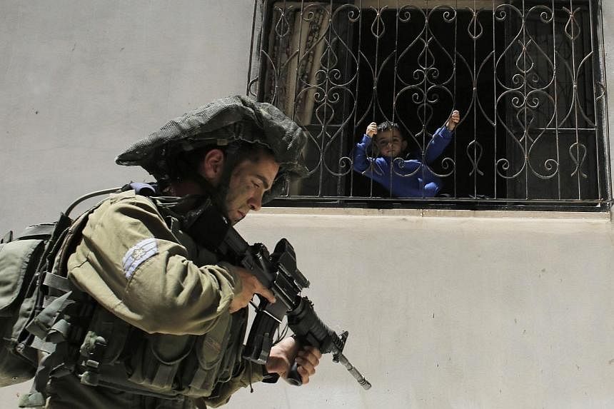A Palestinian boy looks out of his house as an Israeli soldier patrols near the West Bank City of Hebron on June 15, 2014.&nbsp;Hamas militants in Gaza fired dozens of rockets at Israel on Monday, which responded with multiple air strikes in a new es