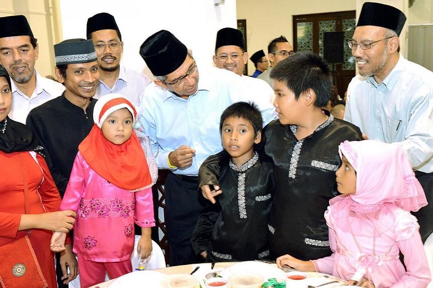 Dr Yaacob Ibrahim (centre, in white), with cleaner Abdullah Arbaa, 41; (third from left, in black), his wife (in red); and their four children. They were at a Ramadan bonus disbursement ceremony held at Muis' premises yesterday.