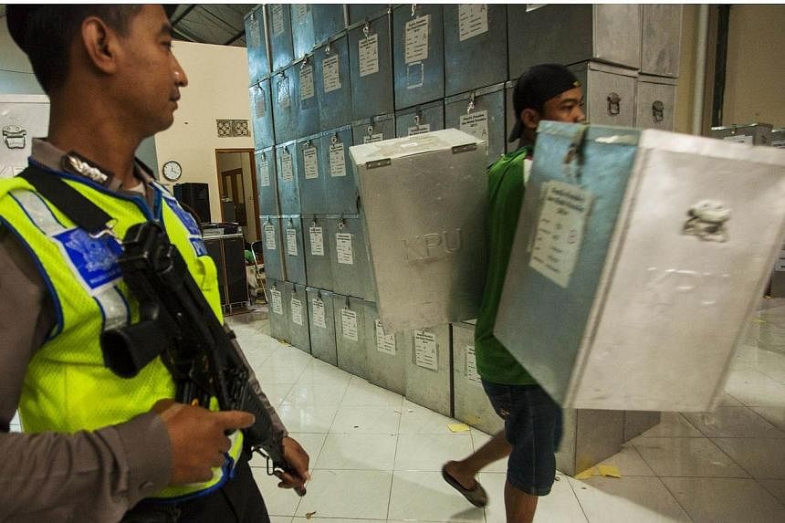 An armed Indonesian policeman watches as a worker carries ballot boxes for distribution to election centers, at the Commission on Election in Yogyakarta, central Java island on July 7, 2014. -- PHOTO: AFP