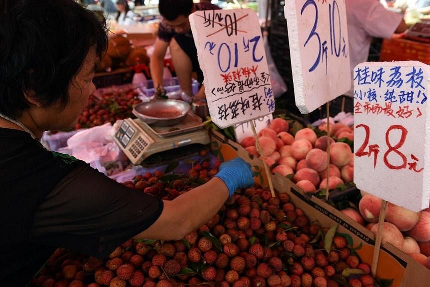 A vendor sorts lychees next to signs showing the prices of various fruit at an outdoor market in Beijing on July 9, 2014.&nbsp;China's annual inflation slowed to 2.3 per cent in June from a four-month high of 2.5 per cent in May, official data showed