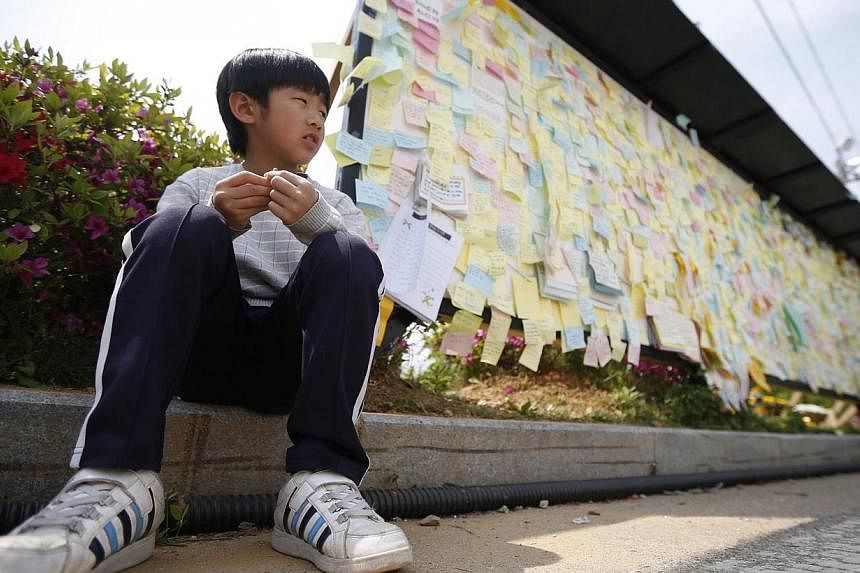 A boy sits next to a board with messages written for victims of sunken passenger ship Sewol, outside the official memorial altar in Ansan May 2, 2014. -- PHOTO: REUTERS