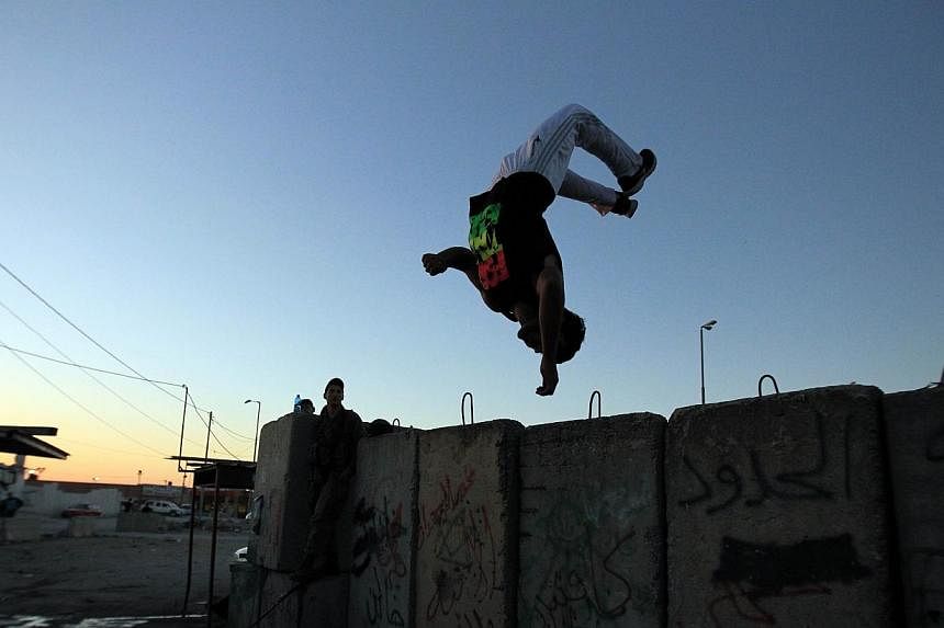A Palestinian jumps in the air showing his parkour skills at the Israeli built controversial separation barrier and Qalandia checkpoint on July 11, 2014. -- PHOTO: AFP&nbsp;