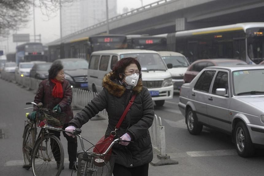 A woman (centre) wearing a mask stands besides her bicycle as vehicles stop at a traffic junction on a busy street amid thick haze in Beijing on Feb 25, 2014.&nbsp;China's capital city, Beijing, will enforce the use of cleaner low-sulphur coal from A