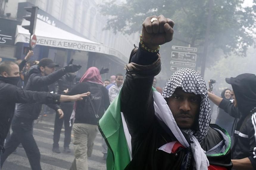 A protester wearing a kaffiyeh and wrapped in a Palestinian flag raises his fist on July 13, 2014 in Paris, during a demonstration against Israel and in support of residents in the Gaza Strip, where a six-day conflict has left 166 Palestinians dead.&