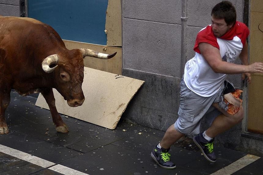 An injured runner is chased by a Miura fighting bull at Estafeta corner during the eighth running of the bulls of the San Fermin festival in Pamplona on July 14, 2014.&nbsp;A bull gored two men after breaking away from the pack and chasing them throu