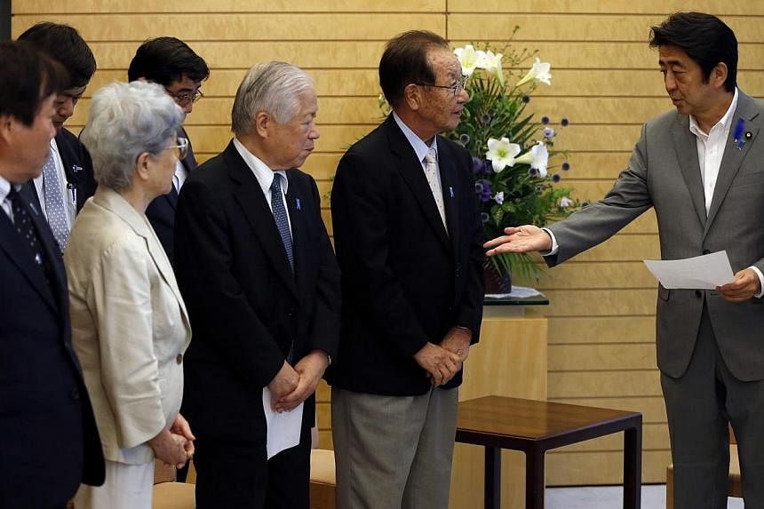 Japan's Prime Minister Shinzo Abe (right) receives a petition from members of abduction issue groups at his official residence in Tokyo on July 4, 2014.&nbsp;As Japan presses North Korea for information on the fate of Japanese citizens abducted decad