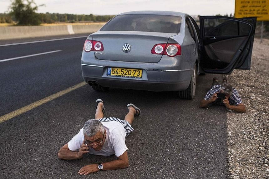 Israelis take cover on the side of a road as a siren sounds warning of incoming rockets outside the northern Gaza Strip on July 15, 2014. -- PHOTO: REUTERS