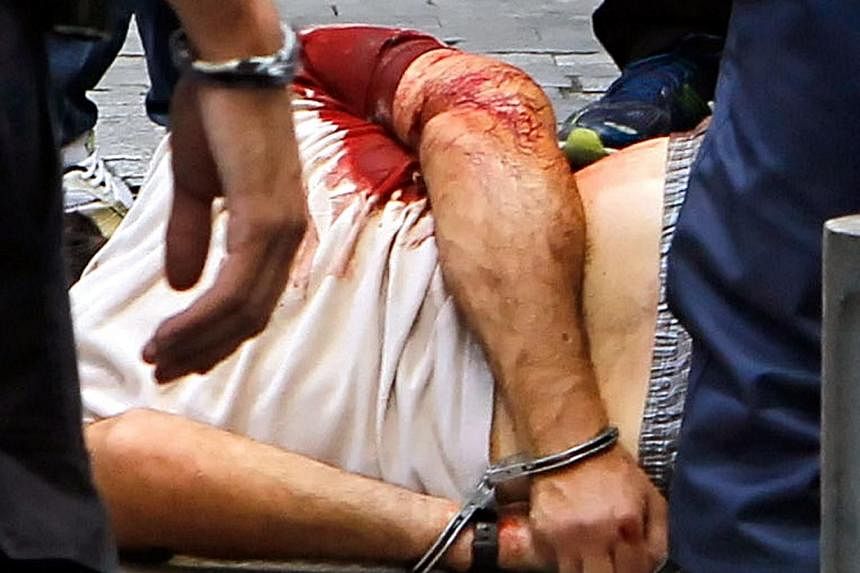 Greek police officers stand next to handcuffed and seriously injured leading member of defunct militant outfit Revolutionary Struggle, Nikos Maziotis, after a shooting in central Athens, in the Monastiraki area, on July 16, 2014. The far-left extremi